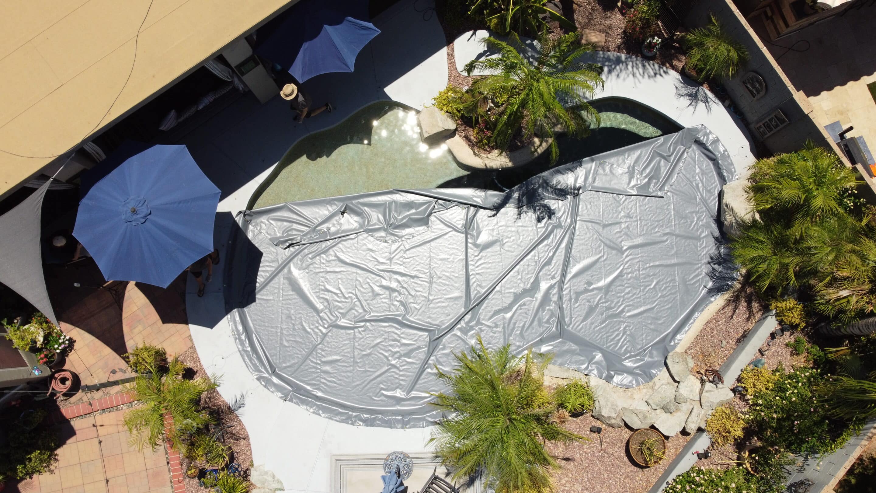 Drone view of two people folding the sides of a PowerLock cover in over the water